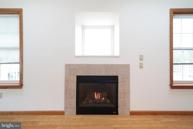 details featuring a tiled fireplace, baseboards, and wood finished floors