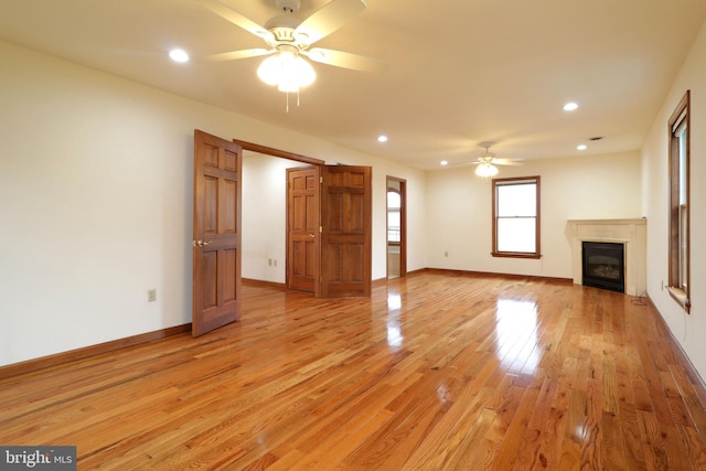 unfurnished living room with a glass covered fireplace, recessed lighting, light wood finished floors, baseboards, and ceiling fan