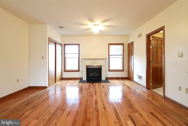 unfurnished living room with light wood finished floors, visible vents, baseboards, and a fireplace with flush hearth