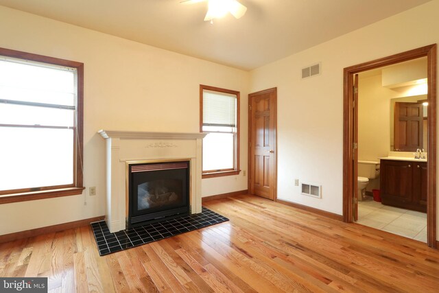 unfurnished living room featuring a tiled fireplace, light wood-style flooring, baseboards, and visible vents