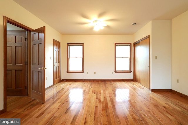 unfurnished bedroom featuring baseboards, multiple windows, light wood-style floors, and a closet