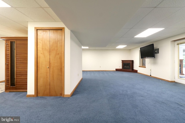 basement featuring a fireplace with raised hearth, a paneled ceiling, baseboards, and carpet floors