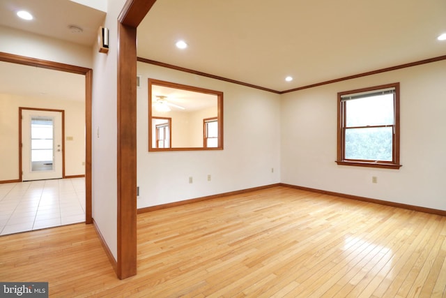 empty room with light wood finished floors, crown molding, and a wealth of natural light
