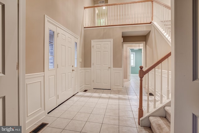 entrance foyer featuring visible vents, a decorative wall, stairway, and light tile patterned flooring