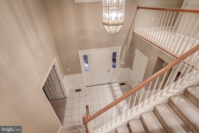 foyer with a wainscoted wall, a decorative wall, a high ceiling, a chandelier, and tile patterned floors