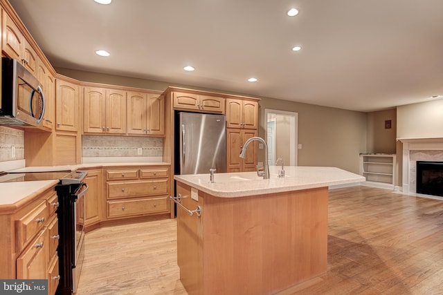 kitchen with light brown cabinets, light wood-style flooring, stainless steel appliances, a sink, and an island with sink