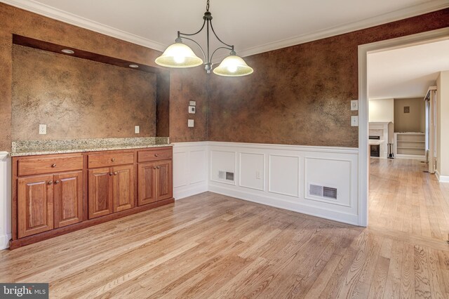 unfurnished dining area with crown molding, a wainscoted wall, visible vents, and light wood-style floors