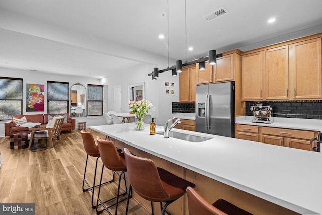 kitchen featuring sink, hanging light fixtures, stainless steel fridge with ice dispenser, light hardwood / wood-style flooring, and backsplash