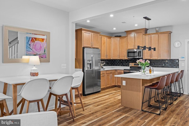 kitchen with hanging light fixtures, decorative backsplash, appliances with stainless steel finishes, a kitchen bar, and kitchen peninsula