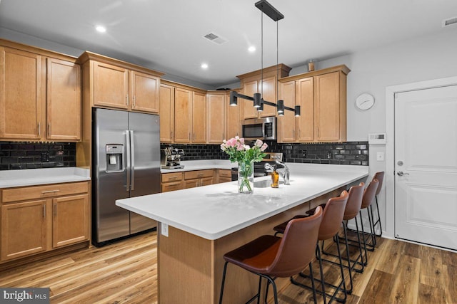 kitchen with kitchen peninsula, stainless steel appliances, decorative light fixtures, light hardwood / wood-style floors, and a breakfast bar area