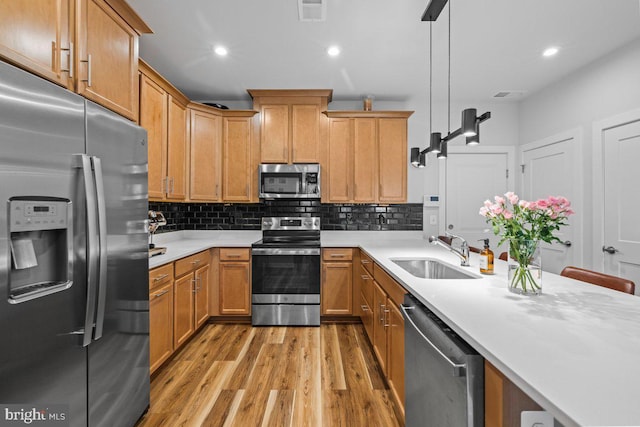 kitchen with sink, tasteful backsplash, light hardwood / wood-style flooring, pendant lighting, and appliances with stainless steel finishes