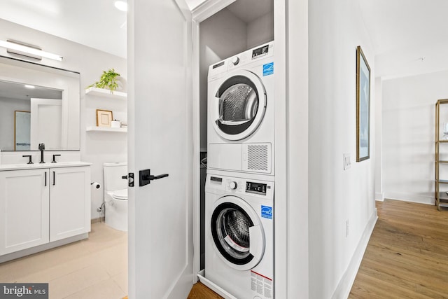 washroom featuring light wood-type flooring, stacked washing maching and dryer, and sink