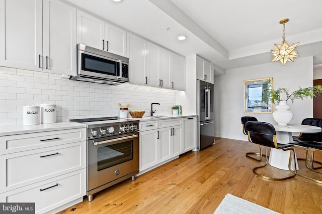 kitchen with white cabinetry, sink, hanging light fixtures, high quality appliances, and decorative backsplash