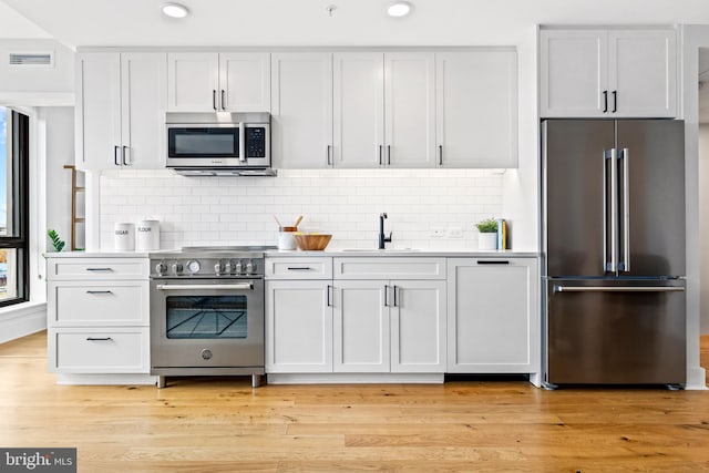 kitchen with light wood-type flooring, backsplash, sink, high quality appliances, and white cabinetry