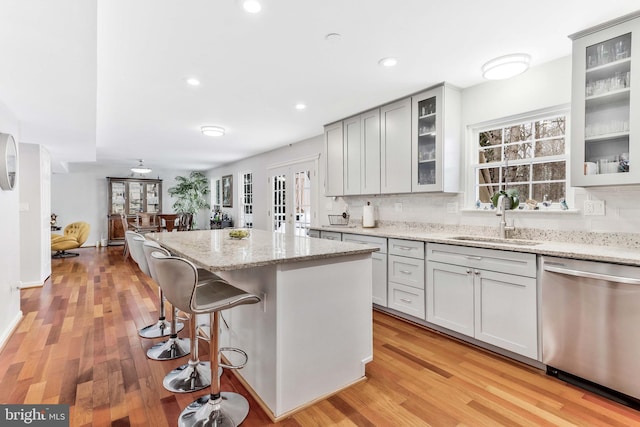 kitchen featuring a kitchen bar, light stone counters, sink, dishwasher, and a center island