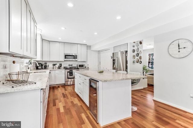 kitchen with sink, stainless steel appliances, beverage cooler, a kitchen island, and white cabinets