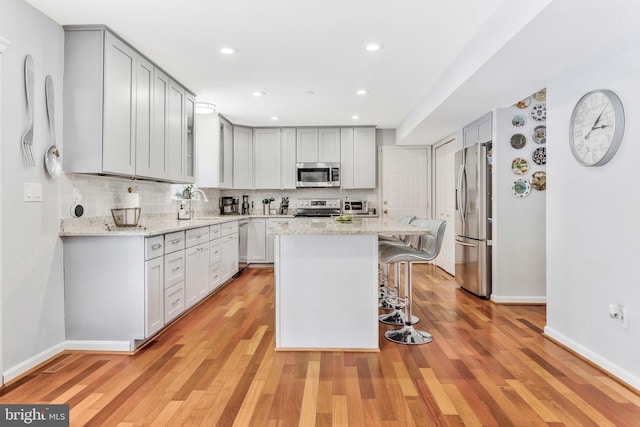 kitchen with light stone countertops, appliances with stainless steel finishes, a center island, and a kitchen breakfast bar