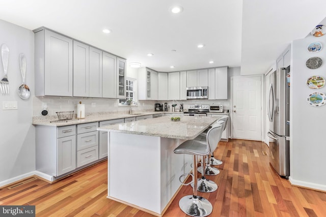 kitchen featuring a breakfast bar area, tasteful backsplash, a kitchen island, light stone counters, and stainless steel appliances