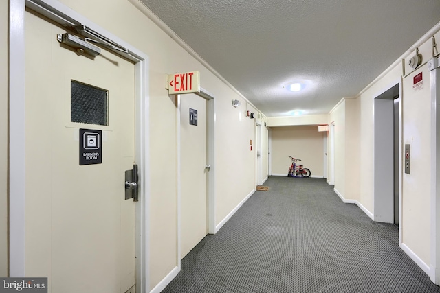 hallway with dark carpet, ornamental molding, and a textured ceiling