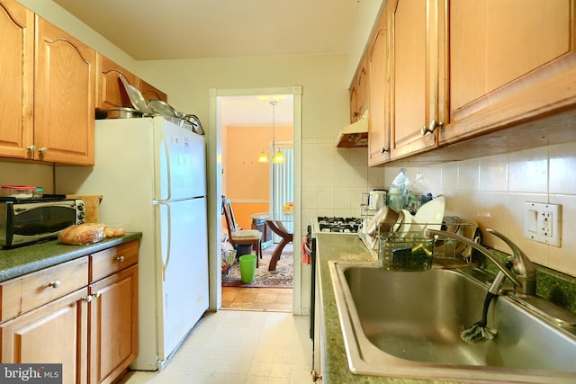 kitchen featuring backsplash, sink, white fridge, and a notable chandelier