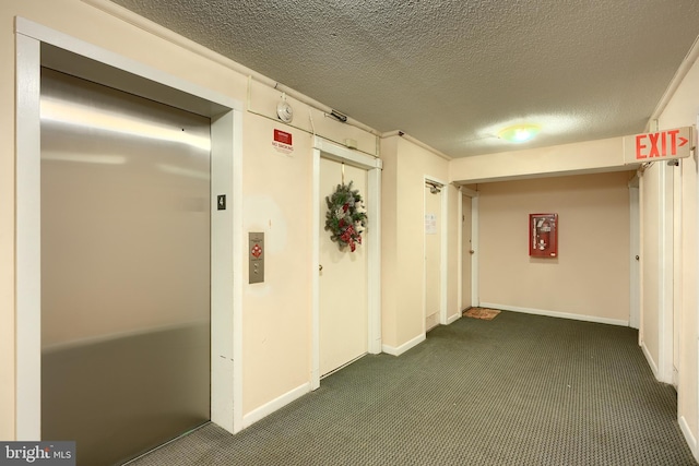 hallway featuring elevator, dark carpet, and a textured ceiling