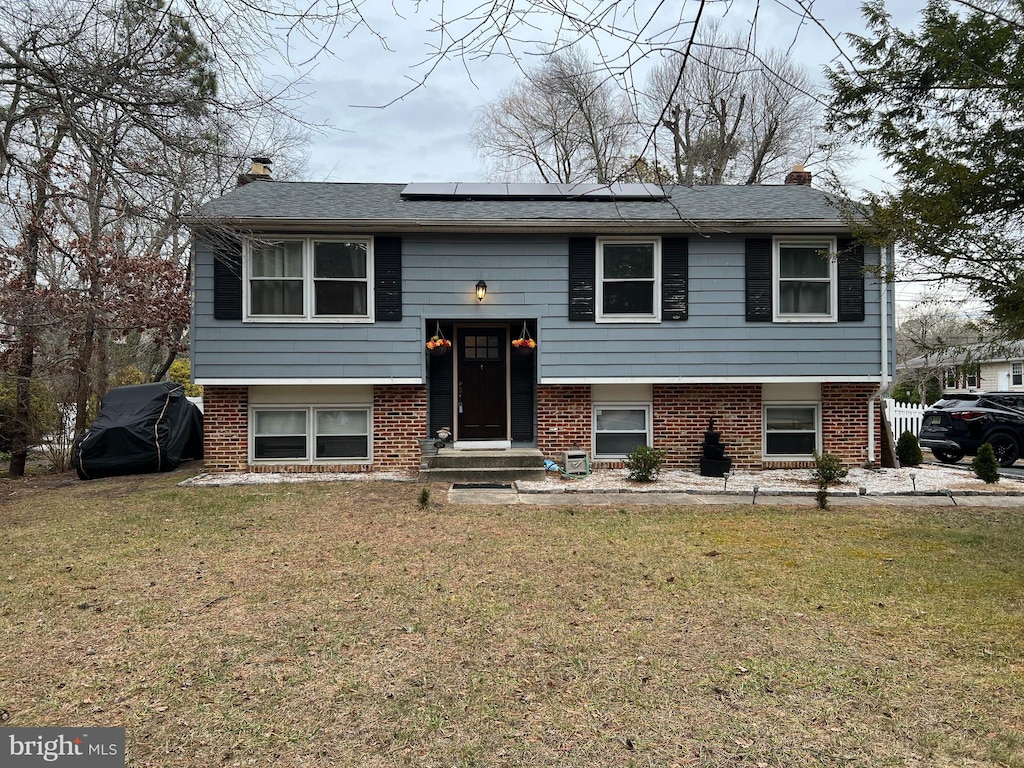 split foyer home with a front lawn and solar panels