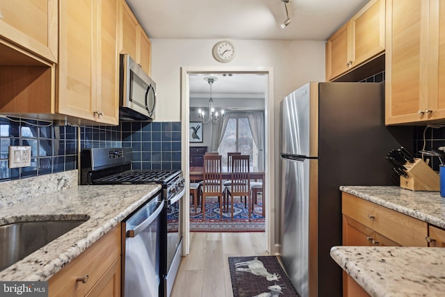 kitchen featuring stainless steel appliances, light stone countertops, decorative backsplash, and light wood-type flooring