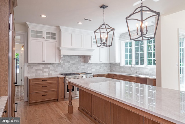 kitchen with double oven range, white cabinetry, sink, and light hardwood / wood-style flooring