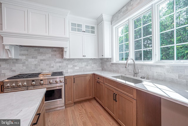 kitchen with sink, light hardwood / wood-style flooring, high end stove, tasteful backsplash, and white cabinetry