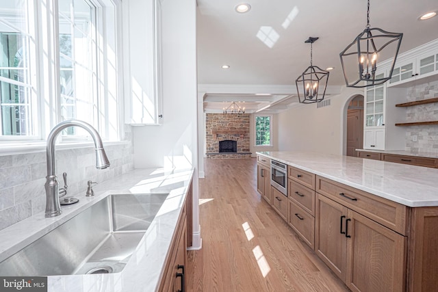 kitchen featuring pendant lighting, sink, light wood-type flooring, a fireplace, and tasteful backsplash