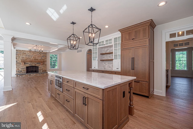 kitchen with a center island, a stone fireplace, hanging light fixtures, built in appliances, and light hardwood / wood-style floors