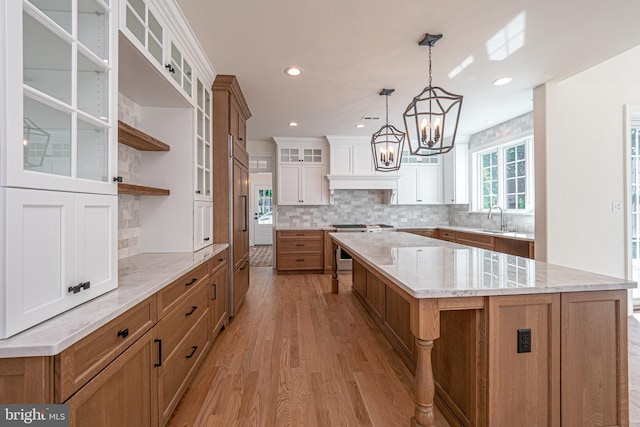 kitchen with pendant lighting, a spacious island, sink, light hardwood / wood-style floors, and white cabinetry