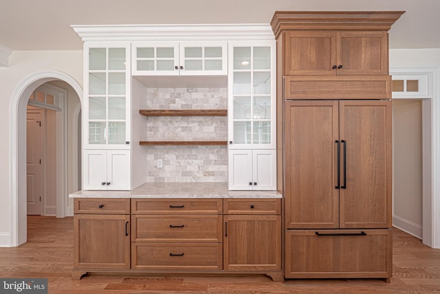 kitchen with decorative backsplash, light hardwood / wood-style floors, light stone counters, and paneled built in fridge