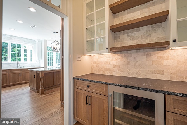 kitchen featuring light wood-type flooring, dark stone counters, beverage cooler, sink, and decorative light fixtures