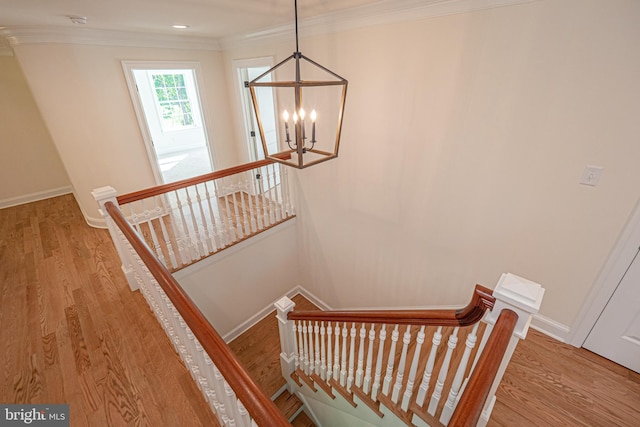 stairs with an inviting chandelier, ornamental molding, and hardwood / wood-style flooring