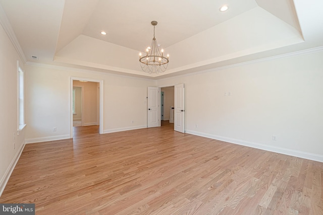 spare room featuring a raised ceiling, an inviting chandelier, light hardwood / wood-style flooring, and crown molding