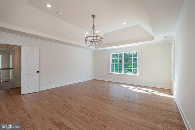 unfurnished room featuring a chandelier, wood-type flooring, a raised ceiling, and ornamental molding