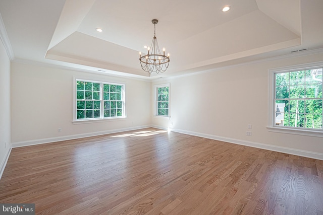 empty room featuring a wealth of natural light, hardwood / wood-style floors, ornamental molding, and a notable chandelier