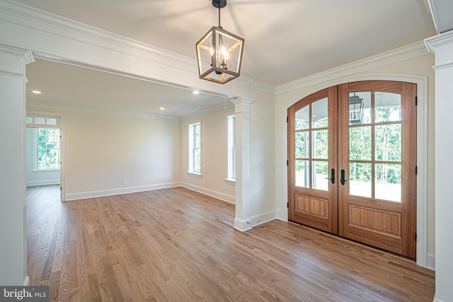 foyer featuring decorative columns, french doors, crown molding, light wood-type flooring, and a chandelier