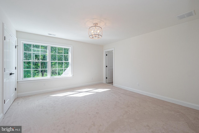 empty room featuring light carpet and a notable chandelier