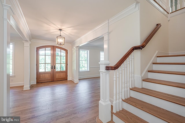 entrance foyer with french doors, an inviting chandelier, ornamental molding, and hardwood / wood-style floors