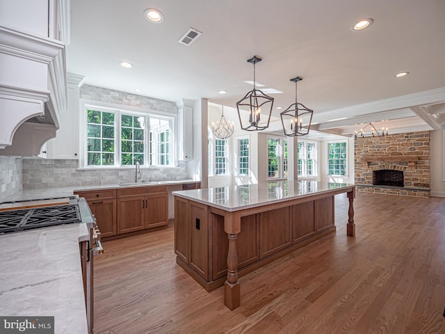 kitchen with light stone countertops, light hardwood / wood-style flooring, a stone fireplace, and a kitchen island