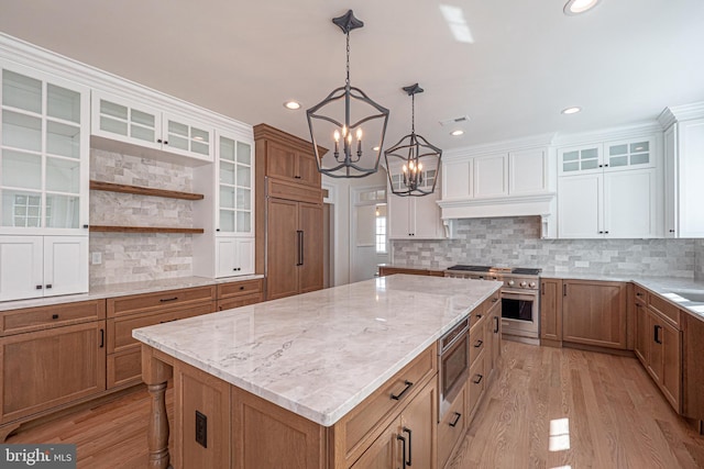 kitchen with built in appliances, a kitchen island, light wood-type flooring, and white cabinetry