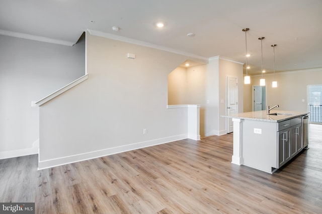 kitchen with light stone counters, crown molding, sink, decorative light fixtures, and a center island with sink