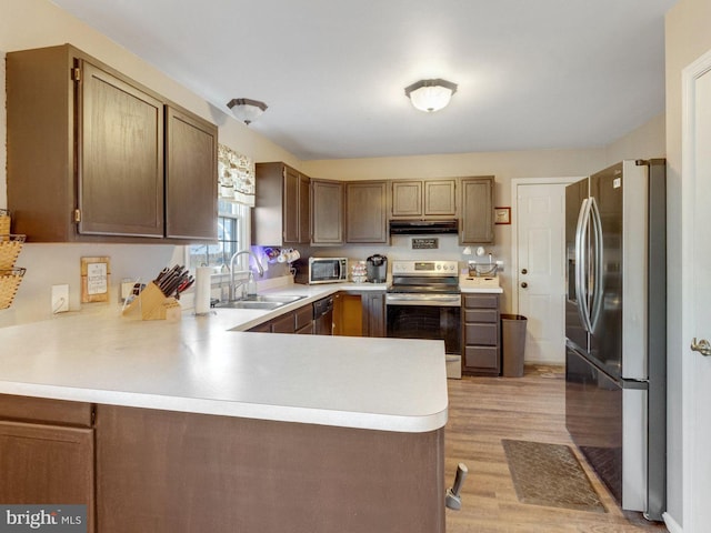 kitchen featuring kitchen peninsula, appliances with stainless steel finishes, light wood-type flooring, and sink