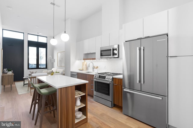 kitchen with a center island, stainless steel appliances, pendant lighting, light hardwood / wood-style floors, and white cabinets