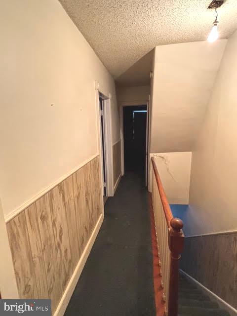 corridor with vaulted ceiling, a textured ceiling, and wooden walls