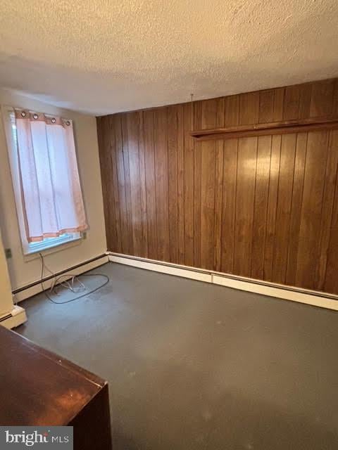 unfurnished room featuring baseboard heating, wooden walls, a textured ceiling, and concrete floors