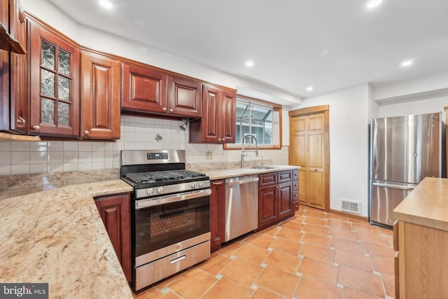 kitchen with appliances with stainless steel finishes, tasteful backsplash, light stone counters, sink, and light tile patterned flooring