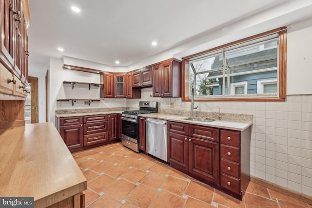 kitchen with light stone counters, sink, stainless steel appliances, and tile walls